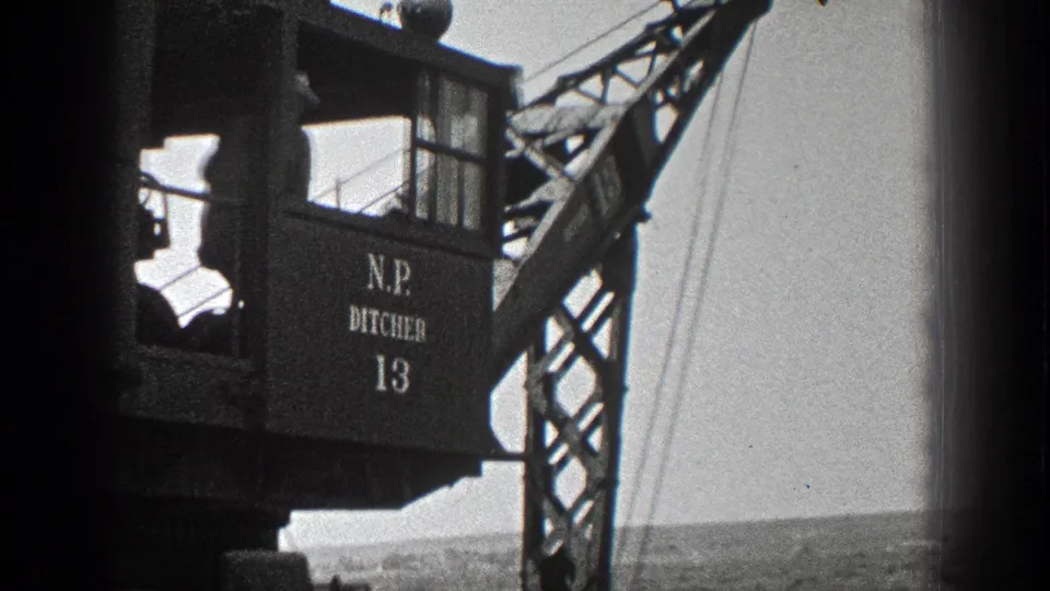 1936 California 8mm frame showing a crane cab with painted "N.P. DITCHER 13" lettering and boom structure near an open shoreline.