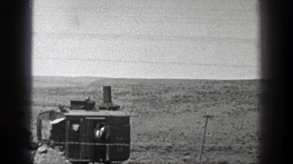 1936 California frame showing the rear of crane machinery on a sandy coastal site, with flat shoreline and pale sky in the background.