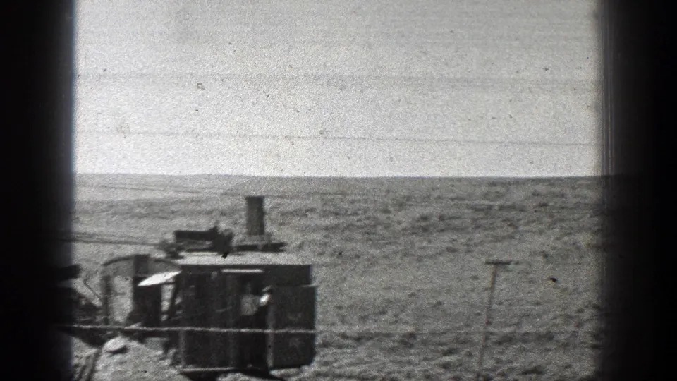 1936 California 8mm frame showing a steam-powered earth mover in an arid landscape, partly framed by dark window or vehicle edges.