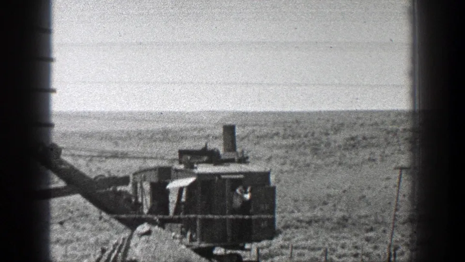 Black-and-white 8mm view of a steam earth mover and boom mechanism in a California desert setting, with a small figure near the cab.