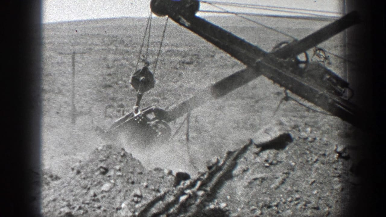 Steam ditcher boom and bucket working over a dusty earth pile in open terrain.