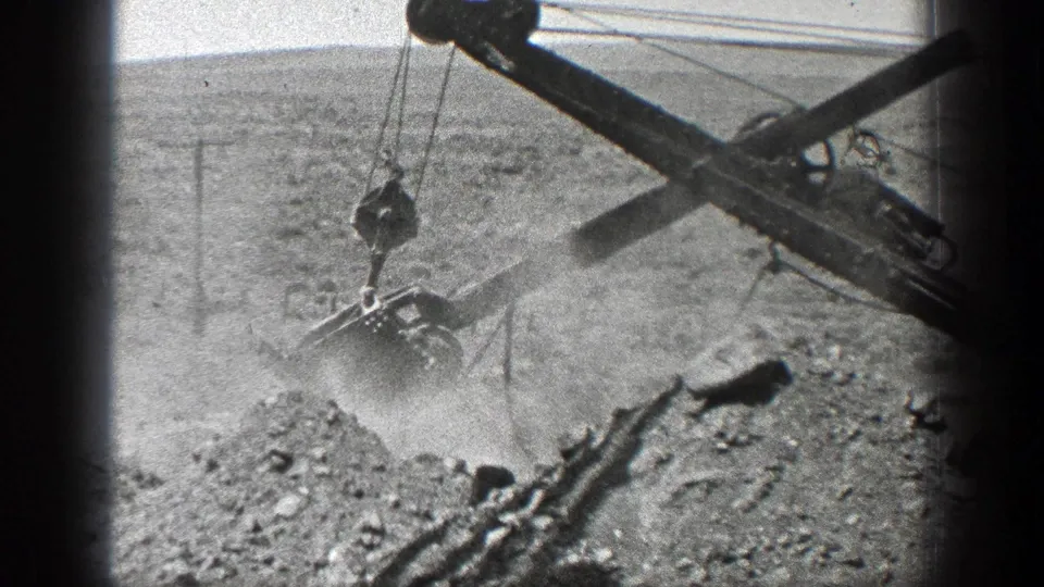 1936 California 8mm frame showing a steam ditcher arm and bucket lifting earth in a rural landscape.