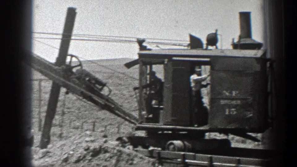 Profile view of the steam ditcher with a worker on the platform and the boom angled across the rural scene.