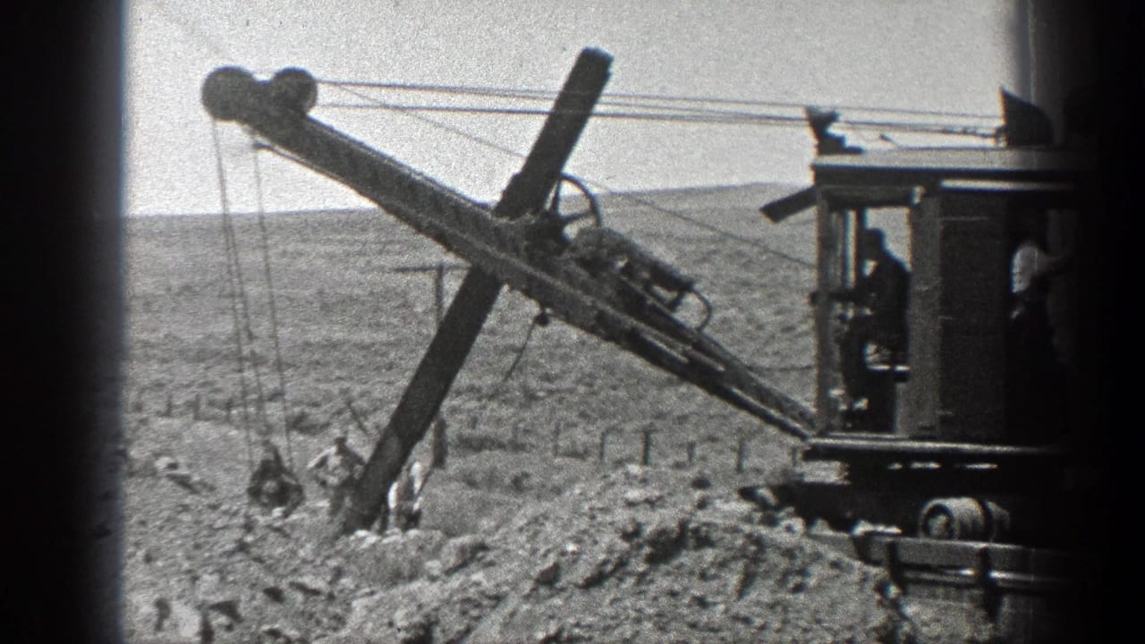Steam drilling machine beside workers and rail materials in a desert worksite.