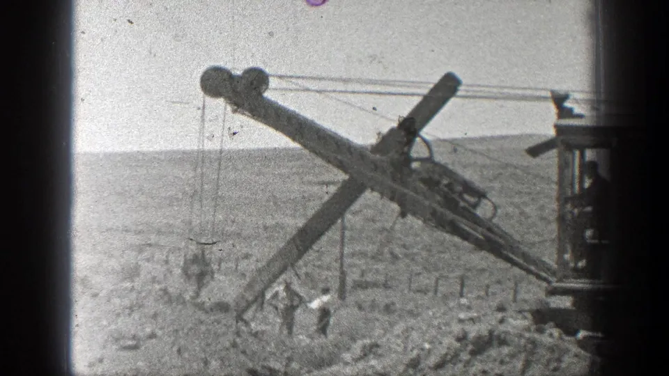 1936 California frame with a drilling machine boom extending over a dusty railroad worksite as laborers stand nearby.