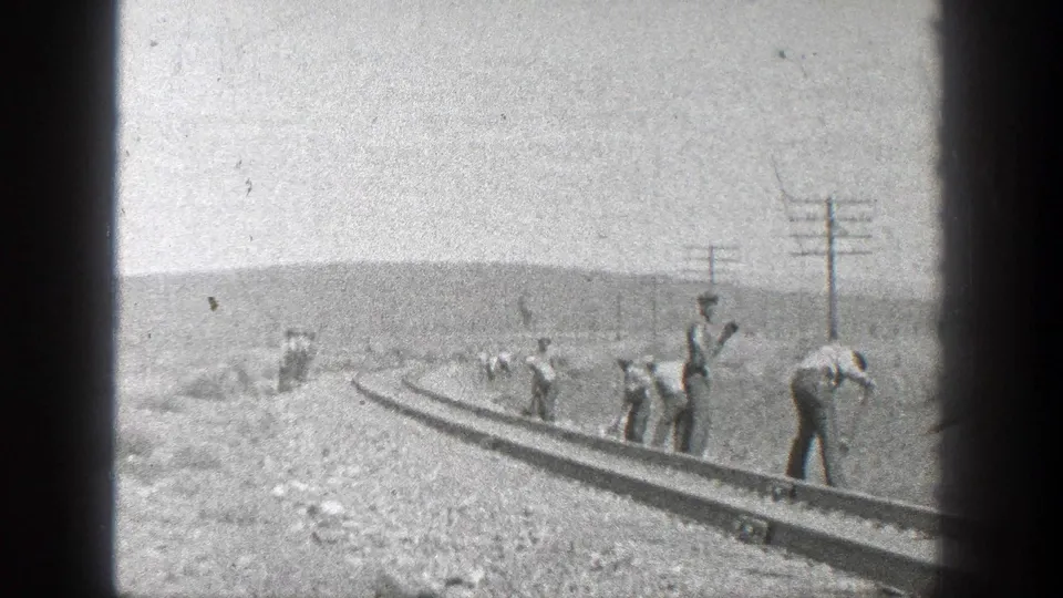 1936 California 8mm view of men working along curved train rails, with utility poles and low hills behind them.