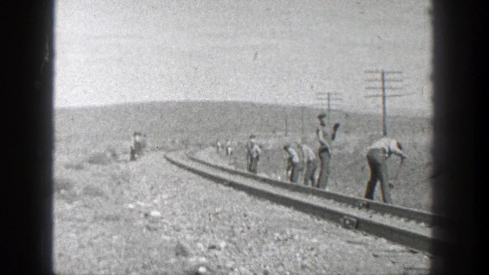 1936 California frame showing railroad workers spaced along curved rails in a dry landscape with telephone or utility poles.