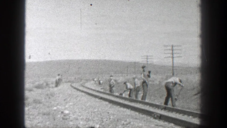 Adult workers maintain a railroad track in rural California, with utility poles and low hills visible in this 1936 8mm home-movie frame.