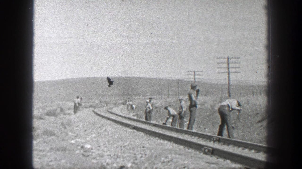 Several workers continue along the rails as a dark bird or speck appears above the track.