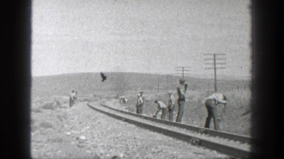 Track workers are spread along a rural California rail line, with poles, low hills, and a dark bird or film speck overhead in the 1936 footage.