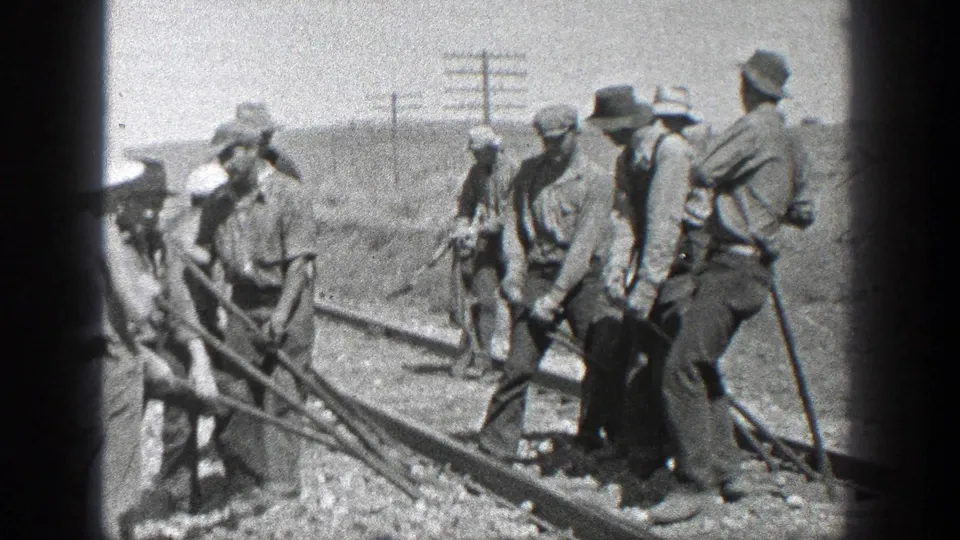 Adult rail workers in hats and work clothes stand close to the track in California, holding long-handled tools during maintenance work in 1936 footage.