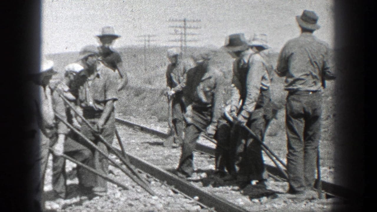 Men in hats work beside railroad tracks with long hand tools in a dry open landscape.