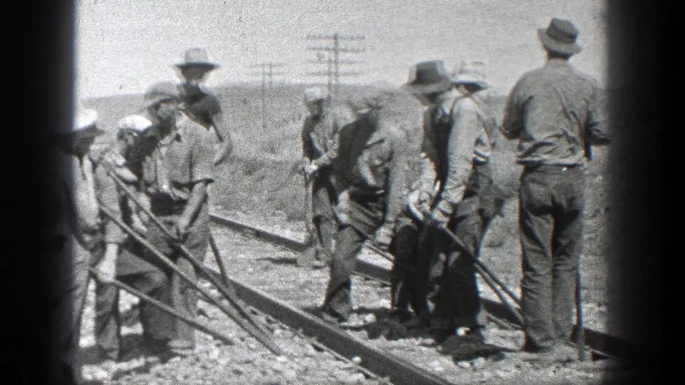 1936 California home-movie frame showing men in hats using hand tools along railroad tracks with utility poles in the background.