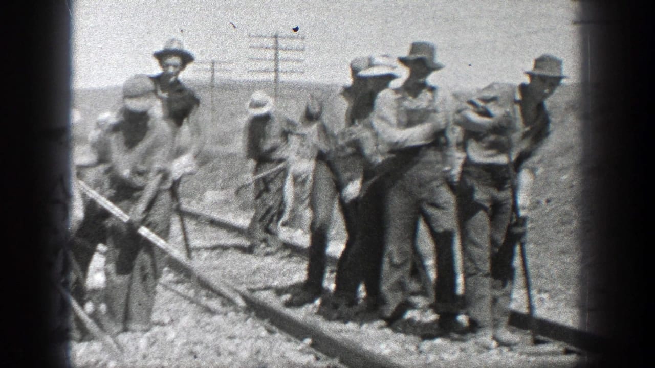 Several men stand and work along railway tracks, some blurred by movement.