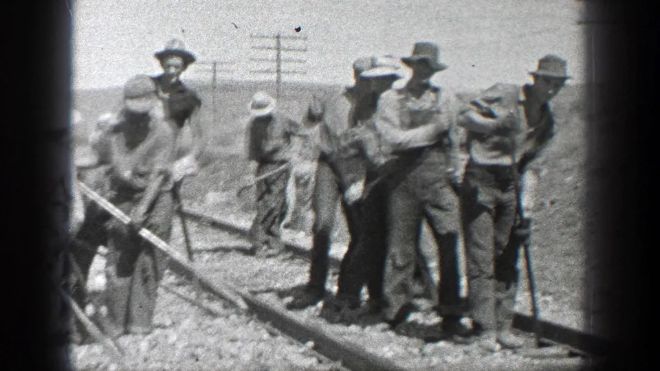 Men in work clothes and brimmed hats appear to maintain railway track in a dry California setting, with utility poles behind them.