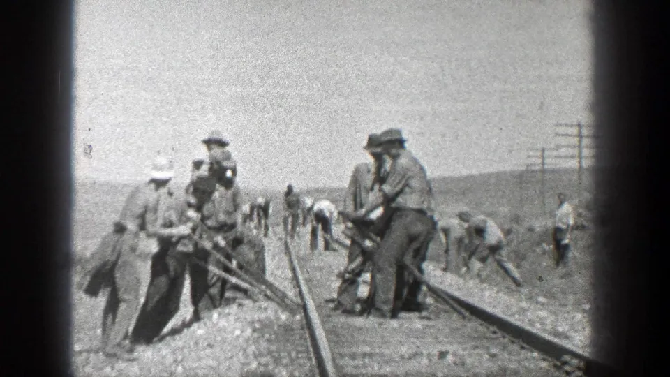 1930s California rail maintenance scene with workers spread along the tracks and foreground men handling long tools on ballast.