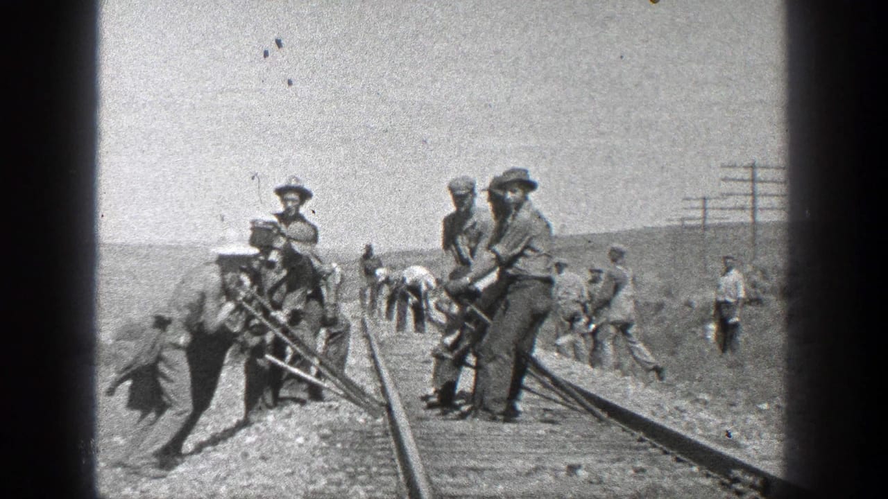 Railroad workers using tools on tracks in an open arid landscape.