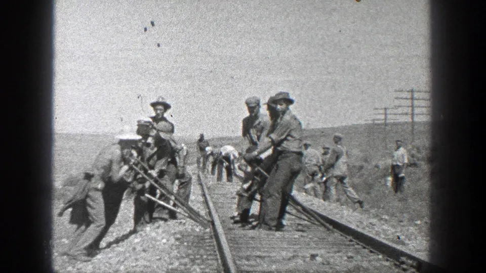 1936 California 8mm frame showing men in hats working with tools on railroad tracks beside utility poles and open hills.