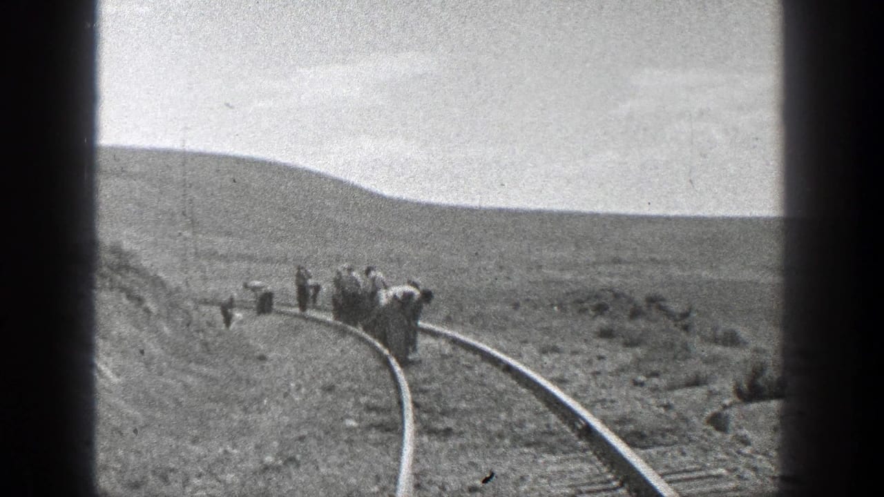 Workers spaced along a curved railroad track in open country.