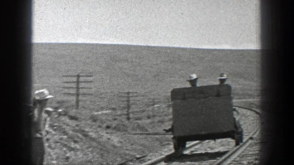 1936 California 8mm frame showing a small rail cart with two men on a curved track near utility poles in dry open country.