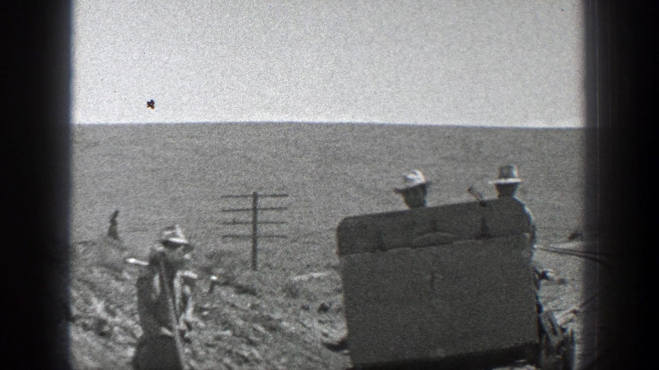 1936 California home-movie frame showing workers around a small rail vehicle on a rural track bordered by utility poles and open terrain.