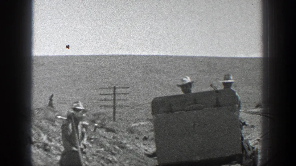1936 California home-movie frame showing workers around a small rail vehicle on a rural track bordered by utility poles and open terrain.