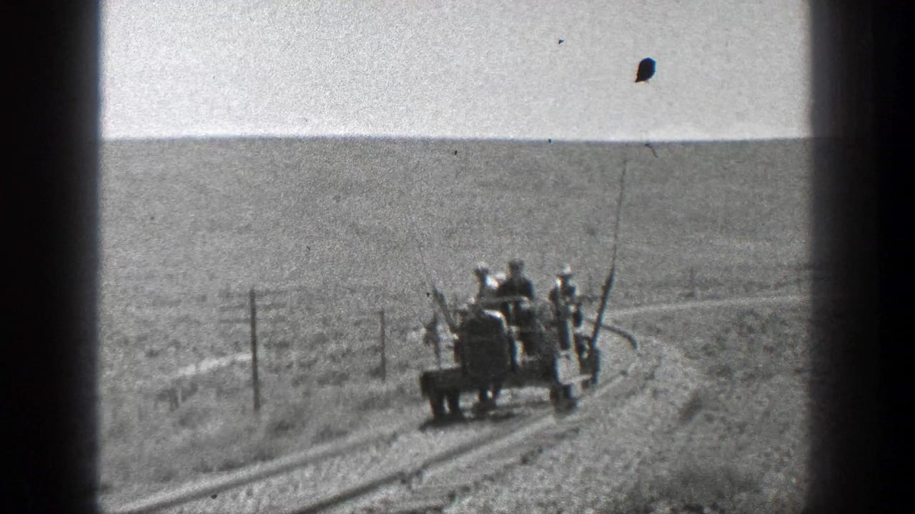 Open rail vehicle carrying several men travels along a narrow rural track beside utility poles.