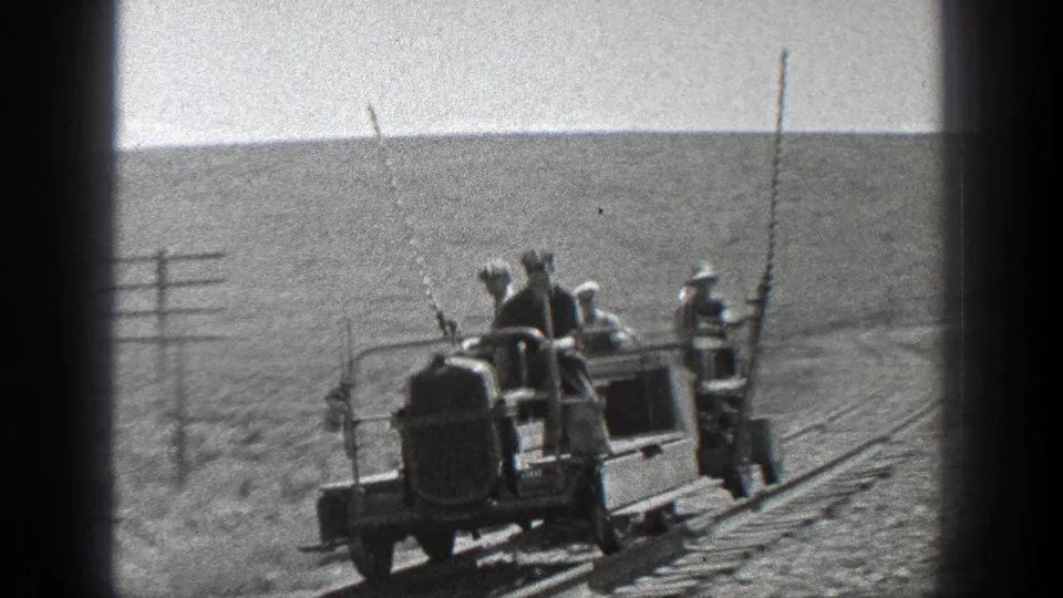 Rear view of workers riding a rudimentary rail cart on a curving rural track in 1936 California, with poles and scrubland visible.