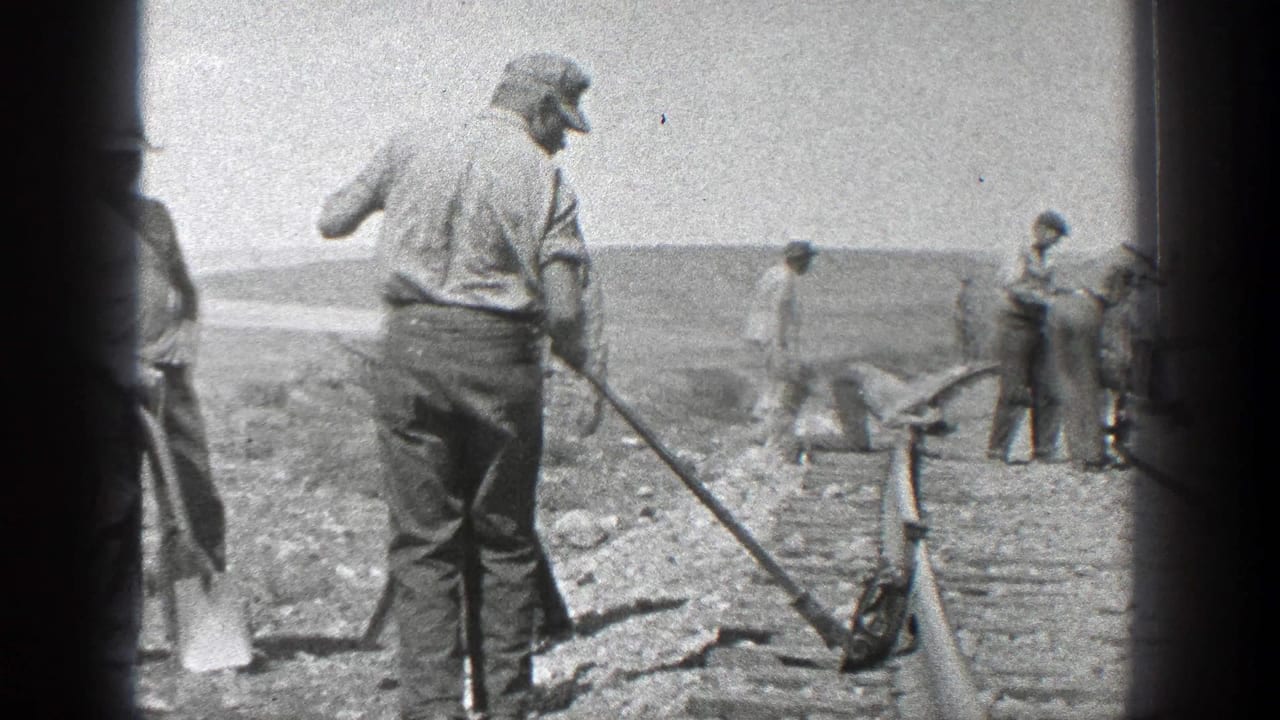 Men work beside a newly laid railroad track in an open landscape.