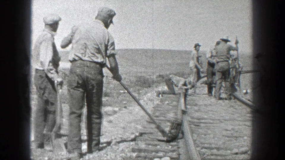 In 1936 California, men in work clothes gather along the rails, with several holding shovels or long tools near the track bed.