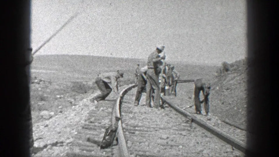 In 1936 California, a line of workers bends and stands along the rail bed while using hand tools on or near the track.