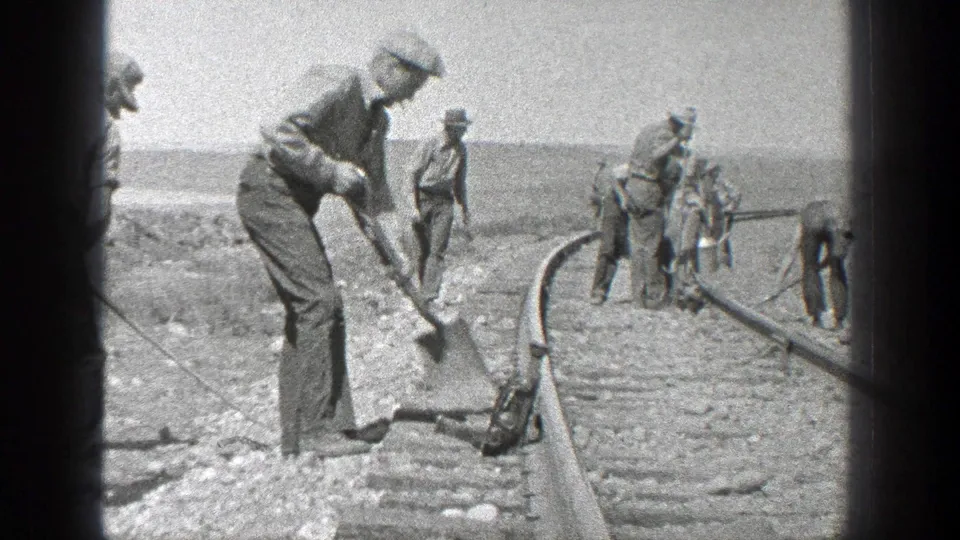 In 1936 California, a foreground worker shovels beside the rail while other men continue track work farther along the line.