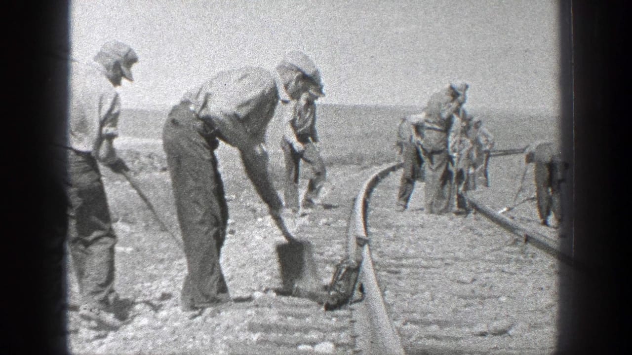 1936 California 8mm frame showing men in hats shoveling and working along railroad tracks in a sunlit open area.