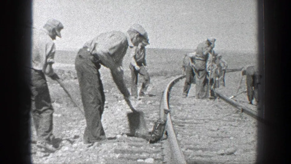 1936 California 8mm frame showing men in hats shoveling and working along railroad tracks in a sunlit open area.