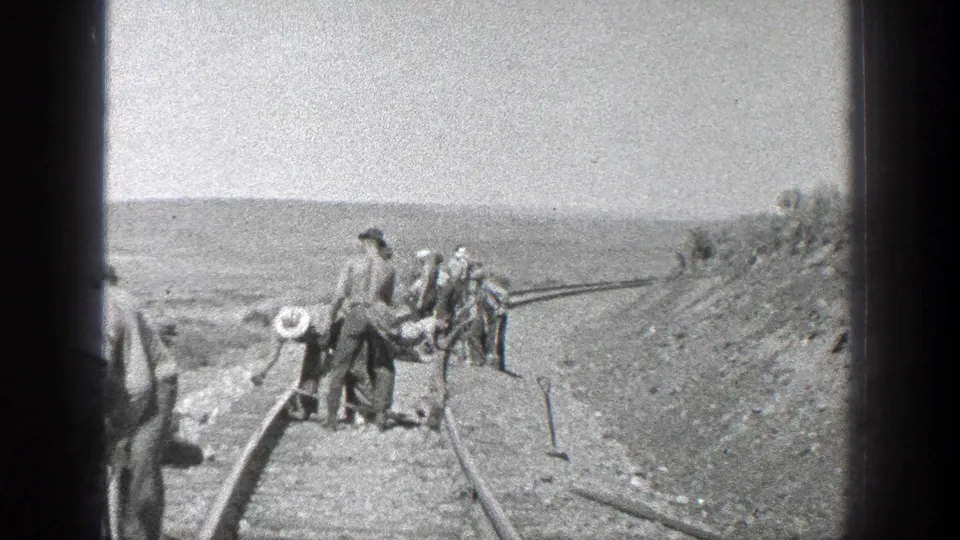 Final black-and-white frame shows workers near railroad rails on a sloped California landscape, with tools and hats visible.