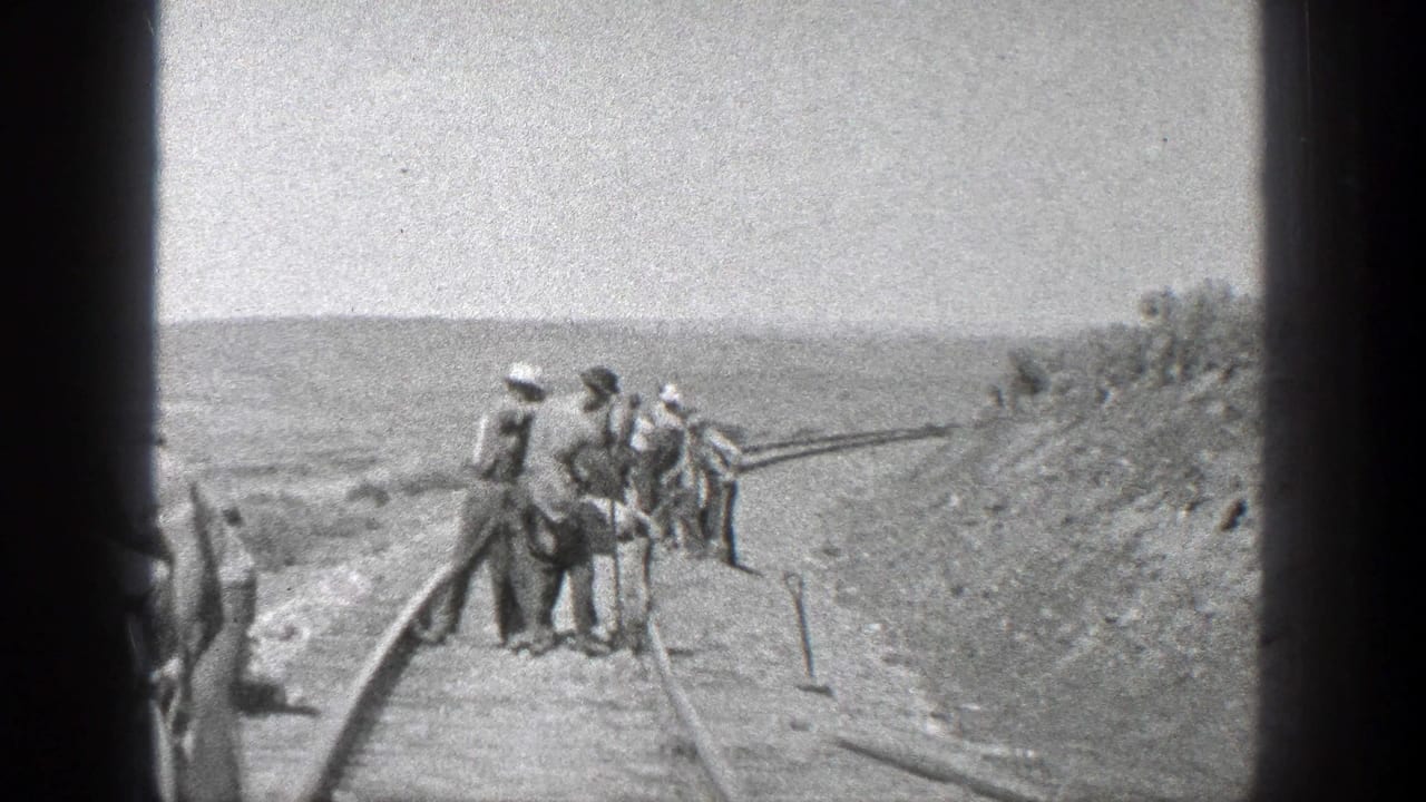 Workers stand and dig beside railroad rails on an open graded track bed.