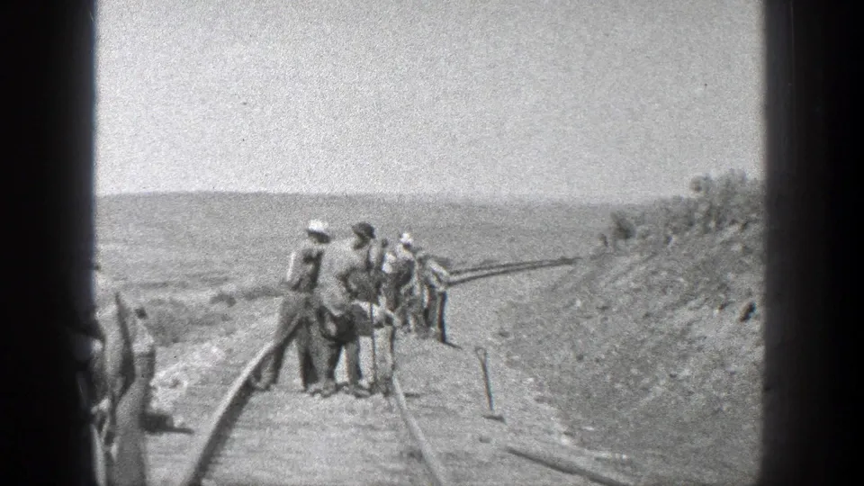 In 1936 California home-movie footage, a small crew of construction workers stands along railroad rails while digging and handling tools on open terrain.