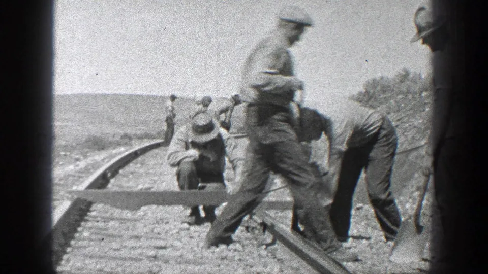 1936 California home-movie frame with men positioned along railroad tracks, some crouching and others standing with tools.