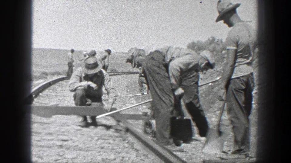1936 California 8mm frame showing railroad workers inspecting or adjusting rails and ties in a dry open setting.