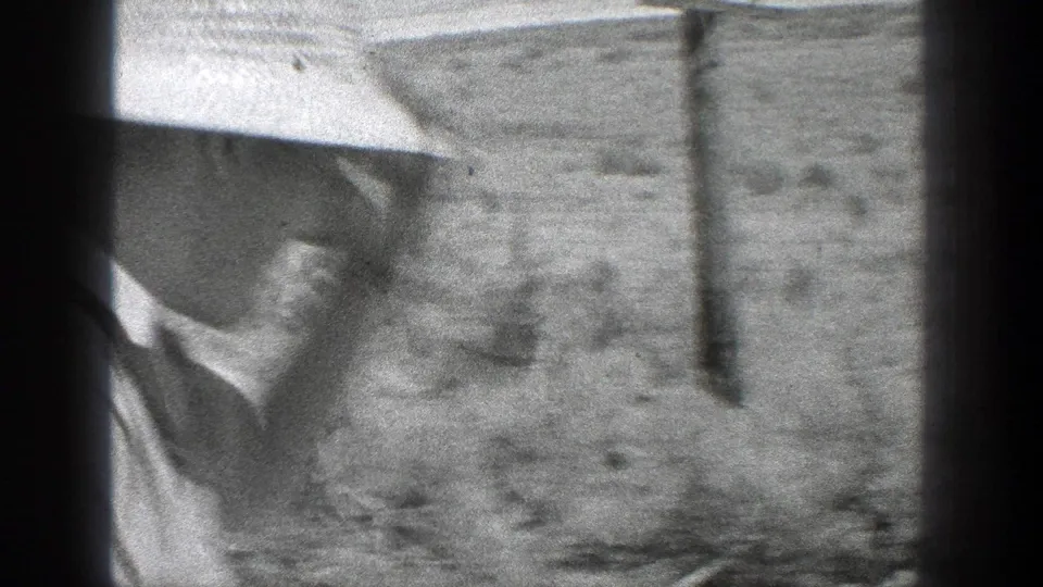 Soft close-up from 1936 California footage showing a worker in a brimmed hat near the rail bed and vertical film-edge shadow.