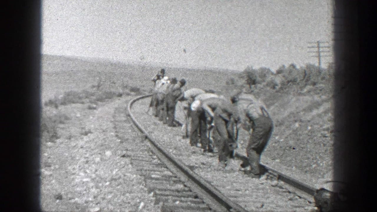 Workers bend along a curved railroad track in an open rural landscape.