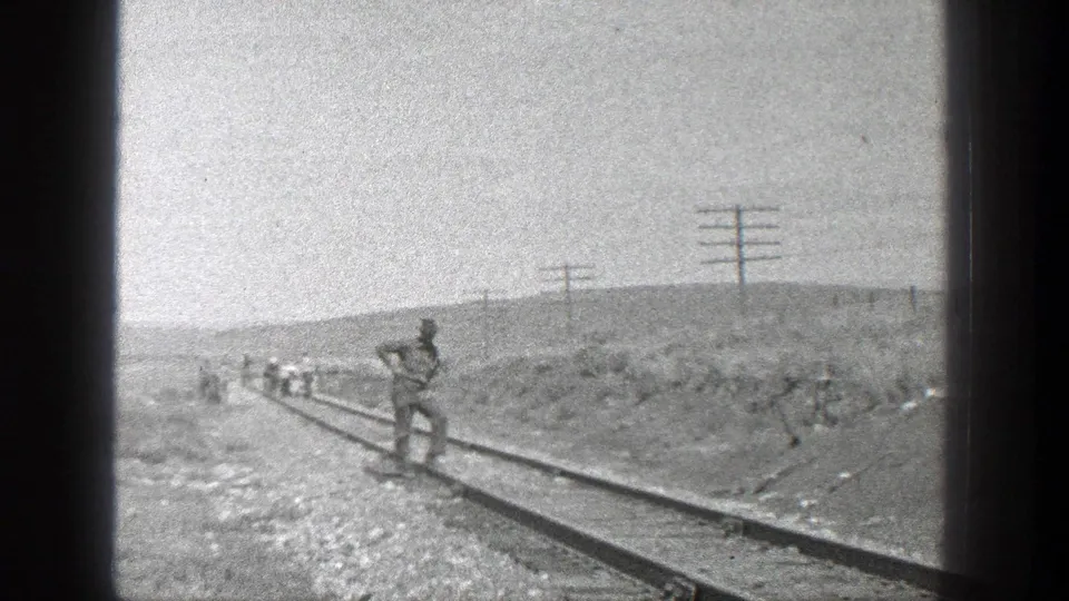 1936 California home-movie frame showing workers on rural railroad tracks with utility poles and low hills in the distance.