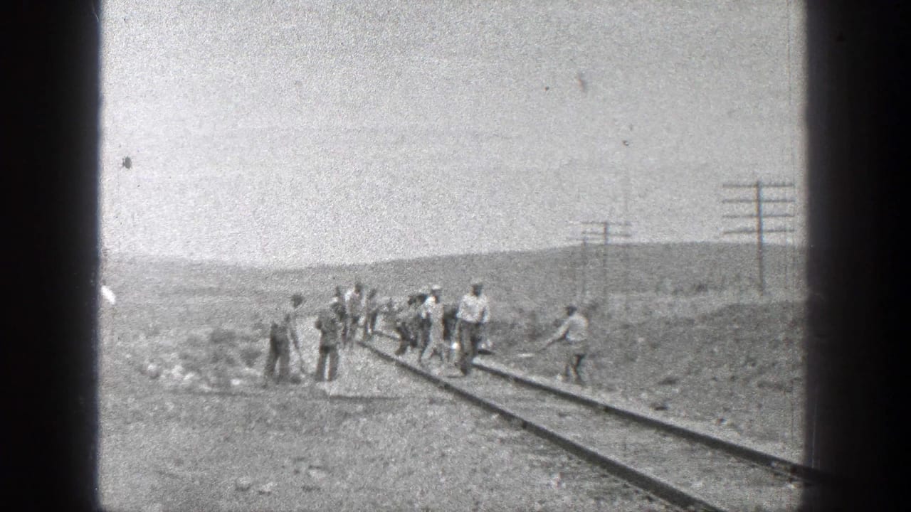 A group of men works beside railroad tracks in open country.