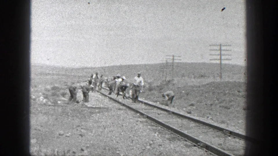 1936 rural California frame showing several men spaced along the rails, some bending toward the track bed.