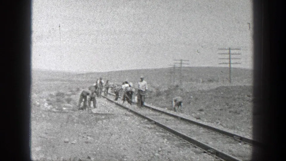 A small crew maintains railroad tracks in a dry California landscape, captured in grainy 8mm monochrome footage.