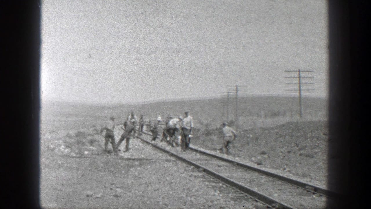 Workers stand and bend over a railway track in an open desert landscape.