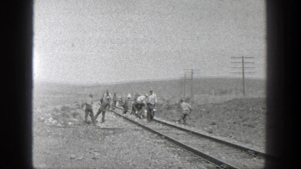 1936 California home-movie frame showing several workers along a railway track with utility poles and low hills in the distance.