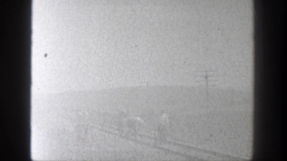 A hazy 8mm frame shows a faint railway scene with workers and poles partly obscured by exposure and film wear.