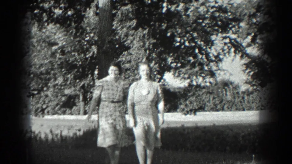 Two adult women in period dresses walk through a sunlit California garden in 1936 home-movie footage.