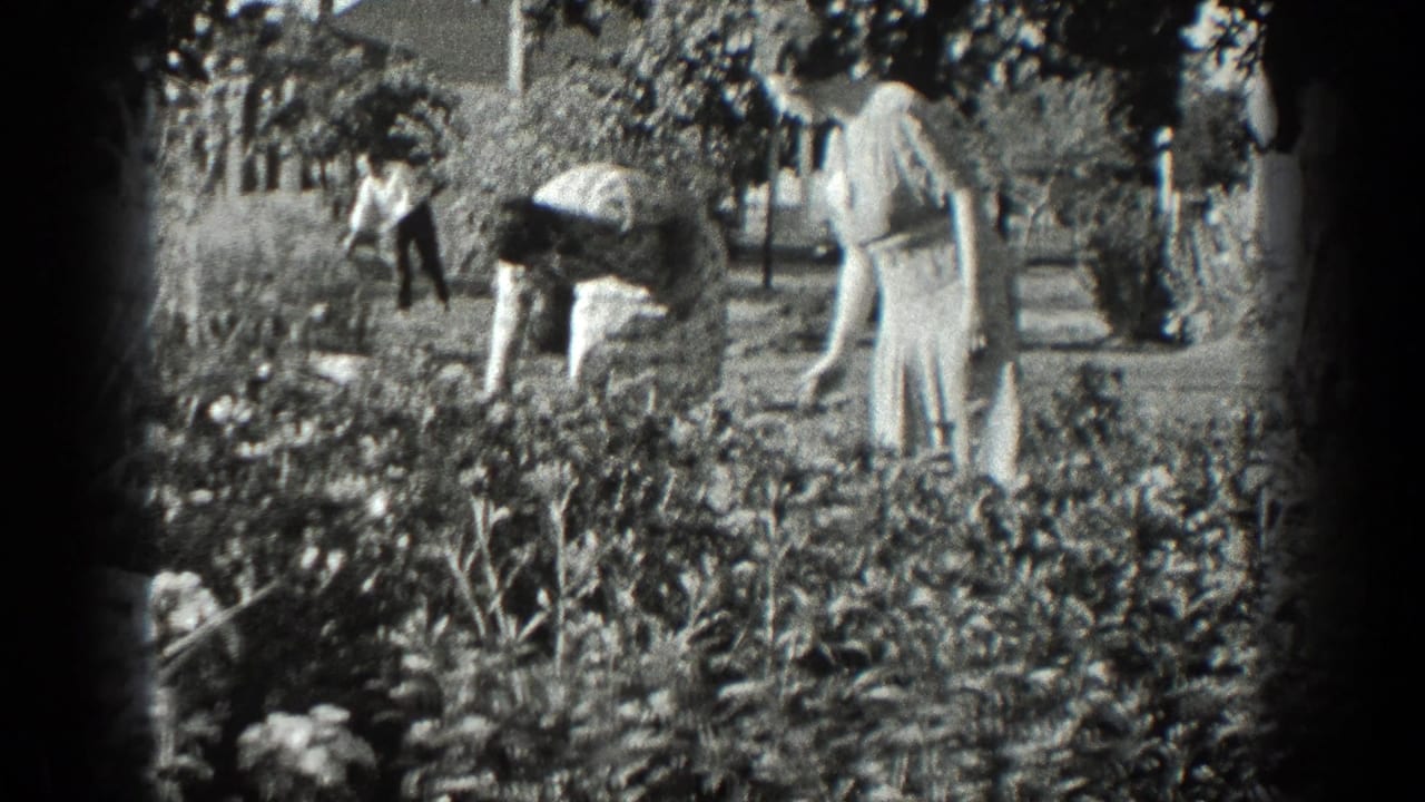 Women in dresses bend over flowerbeds in a garden with houses behind them.